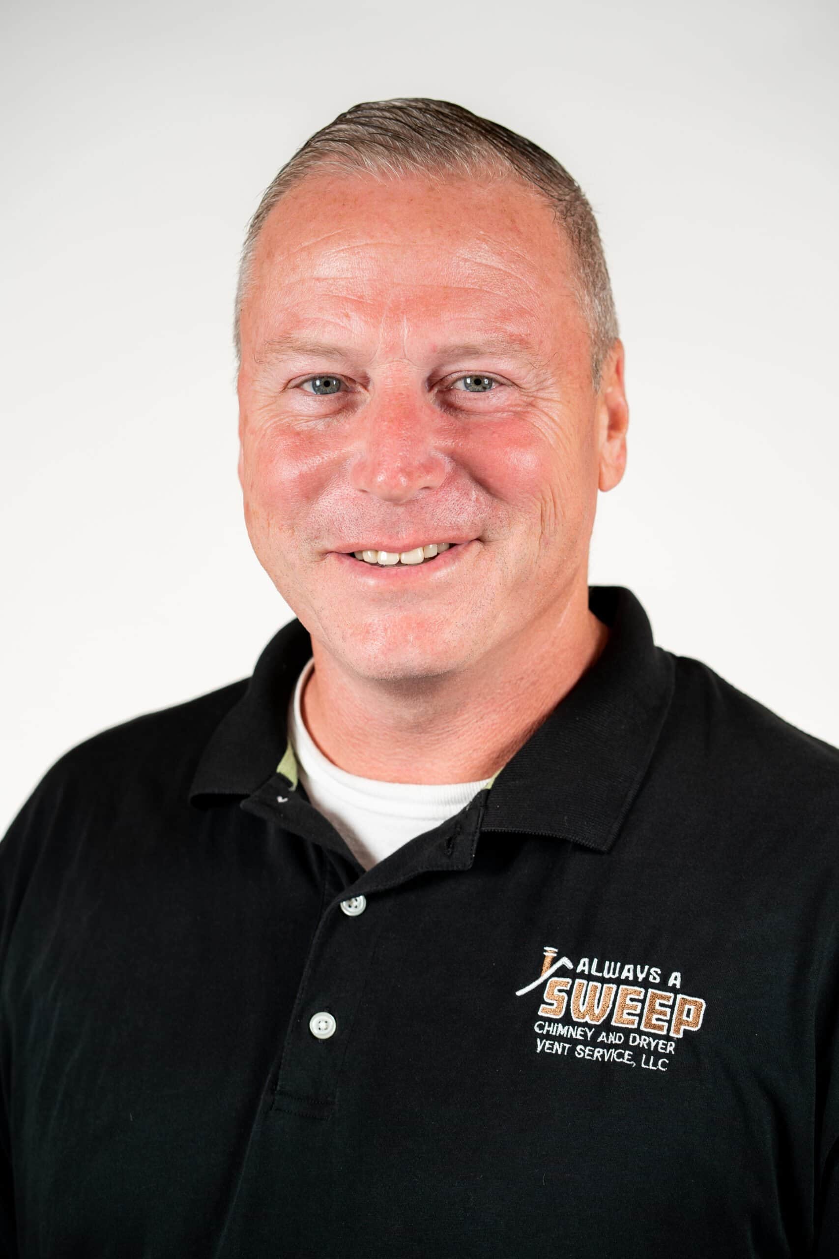 A professional headshot of a smiling man wearing a black polo shirt featuring the 