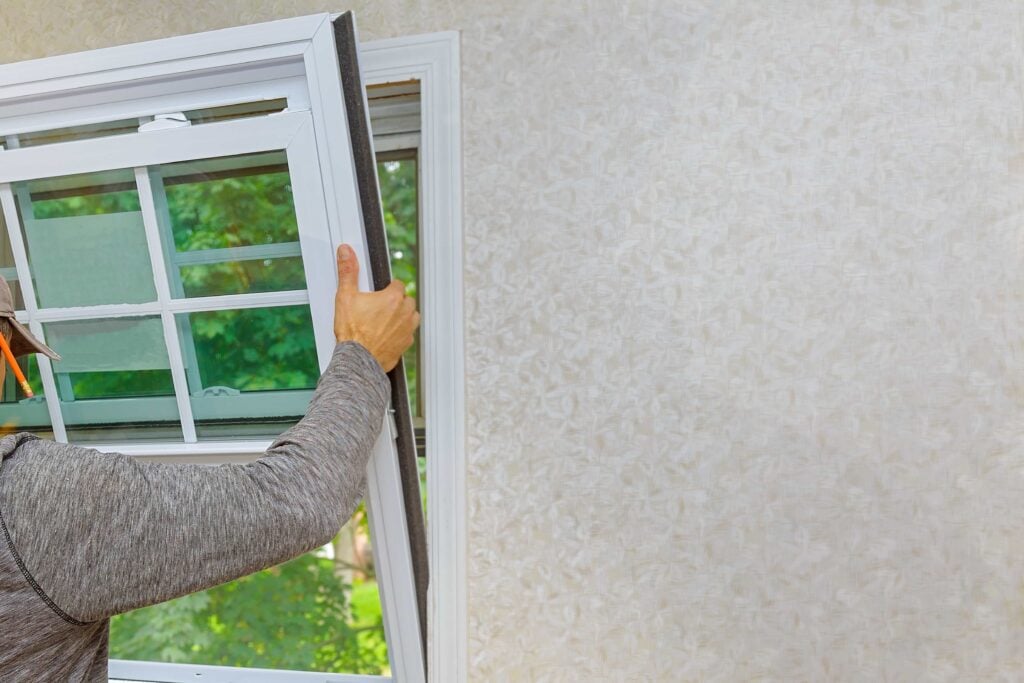Preventative Home Maintenance to Protect Your Florida Property 4 A professional installer fitting a new white vinyl double-hung window frame into a residential wall opening, demonstrating expert impact window replacement service in Miami, Florida.