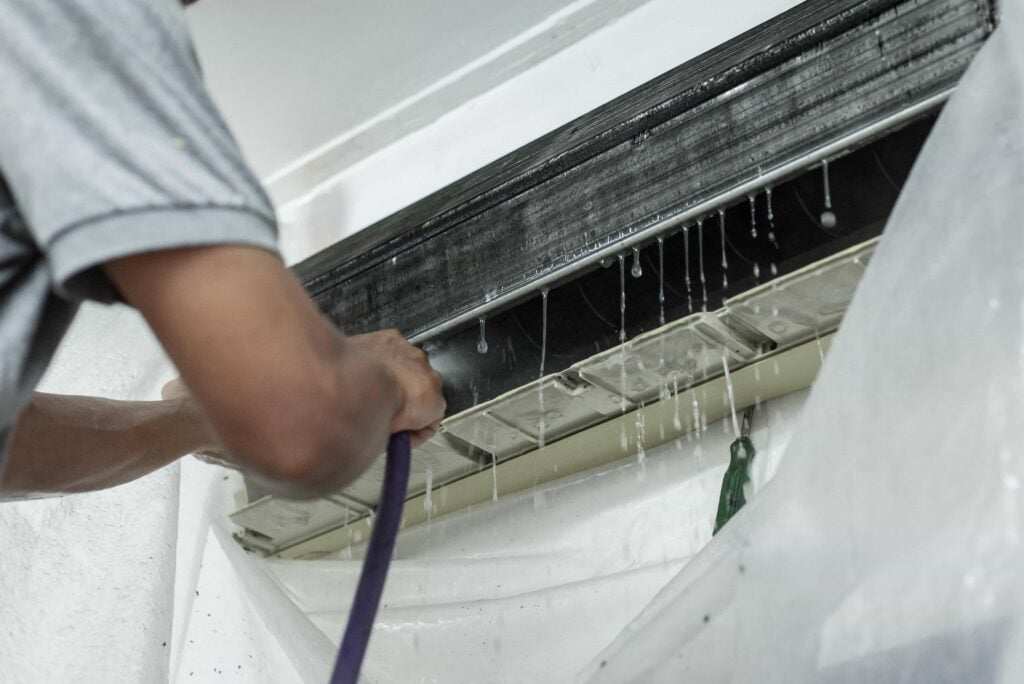 Preventative Home Maintenance to Protect Your Florida Property 3 A technician using a water hose to deep clean the evaporator coils of an indoor mini-split air conditioner unit, showcasing professional AC coil cleaning service in Miami, Florida.