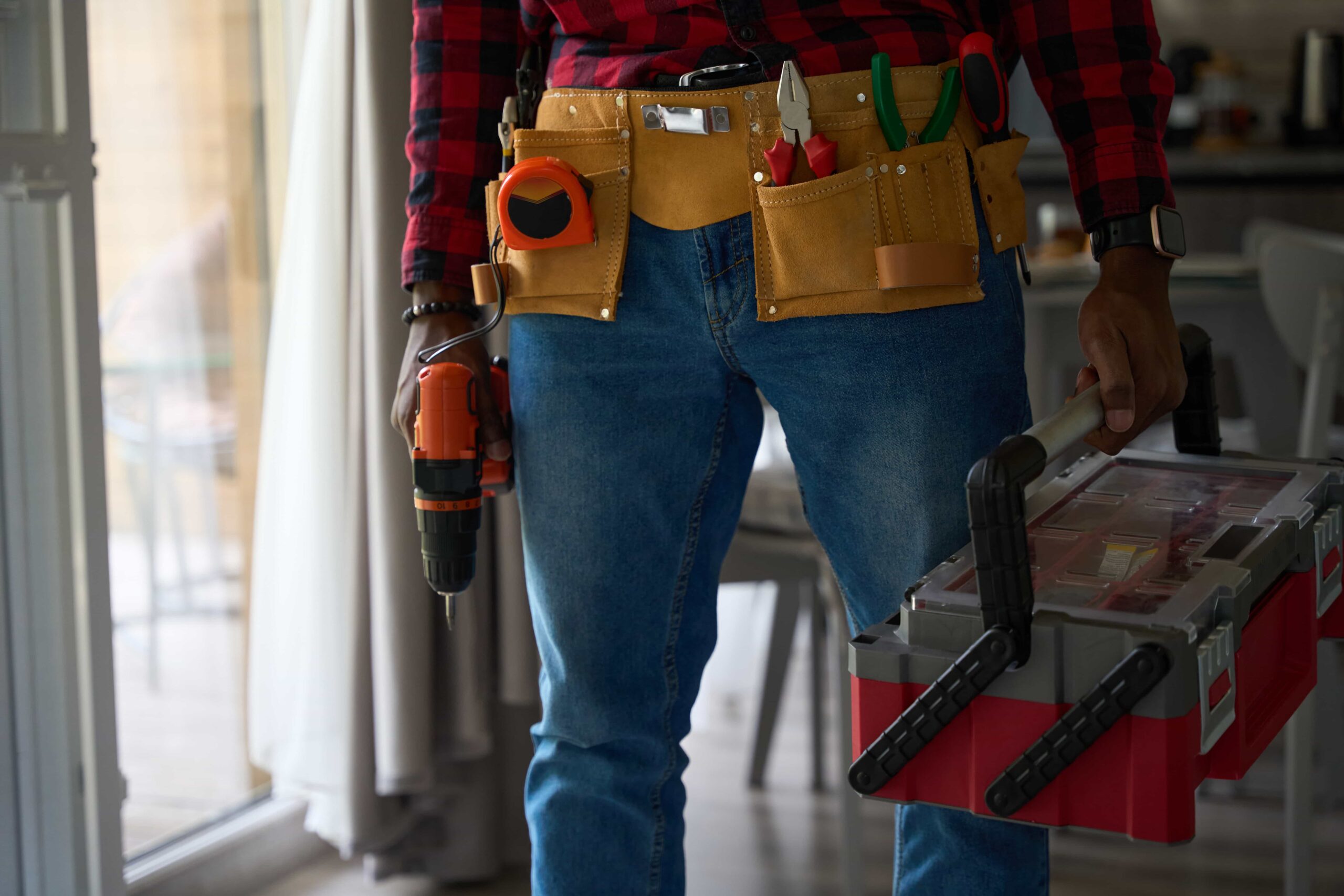 Handyman Repair Services: Save Thousands on Home Maintenance 1 A professional handyman repair services in Atlanta, GA wearing a tool belt and holding a power drill and toolbox indoors.